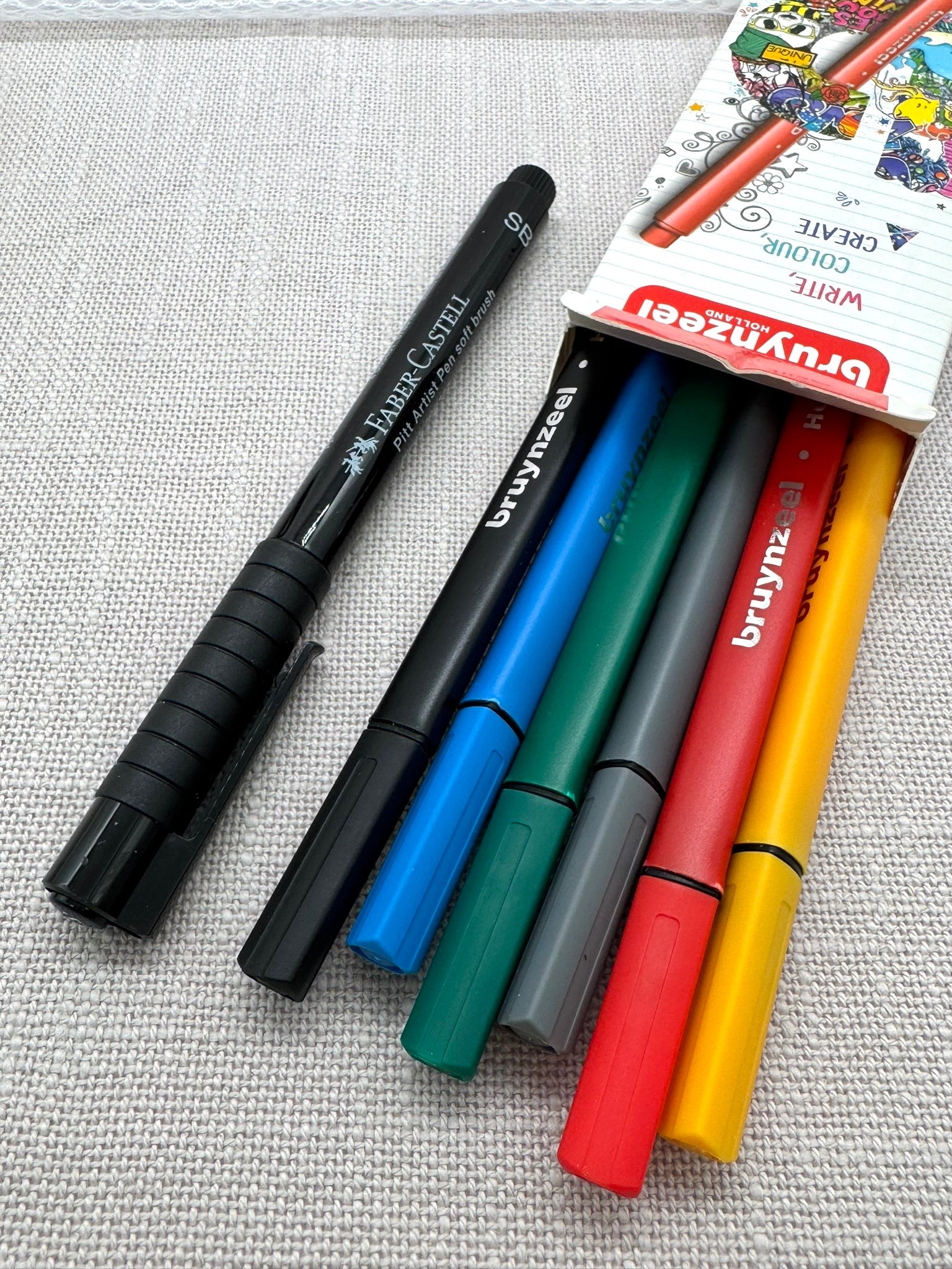 ein Set mit 6 bunten Finelinern in einem Karton und ein schwarzer Faber-Castell Brush Pen