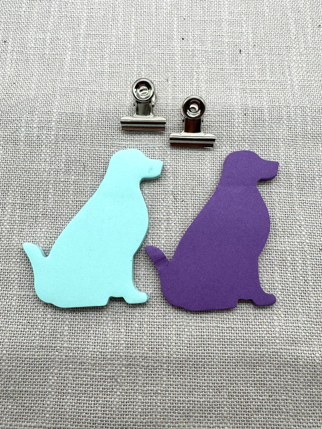 Nahaufnahme der Haftnotizen in Form von einem Labrador. Ein Block mintgrün, ein Block lila. Oben drüber liegen zwei kleine Metallklammern.