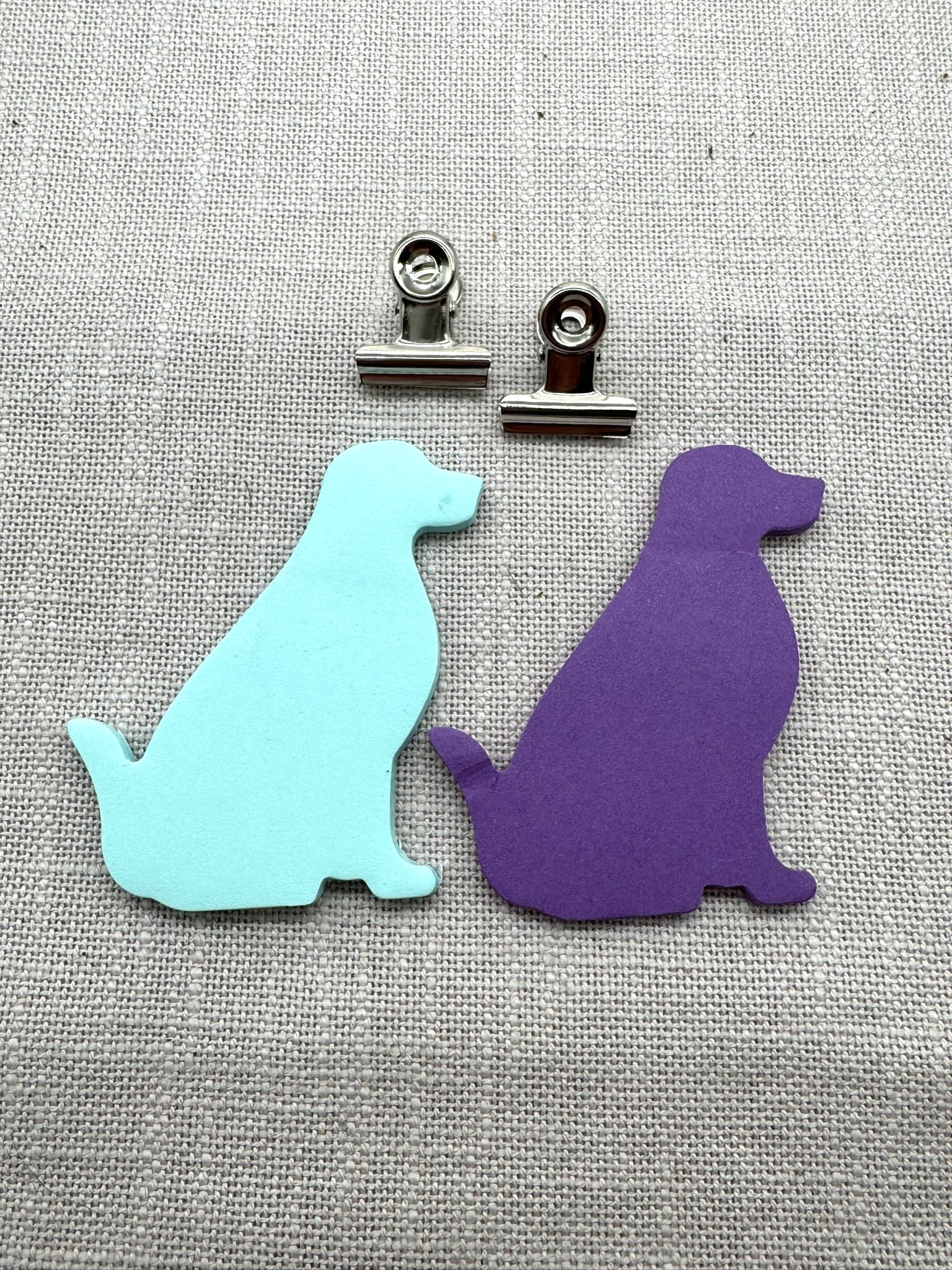 Nahaufnahme der Haftnotizen in Form von einem Labrador. Ein Block mintgrün, ein Block lila. Oben drüber liegen zwei kleine Metallklammern.