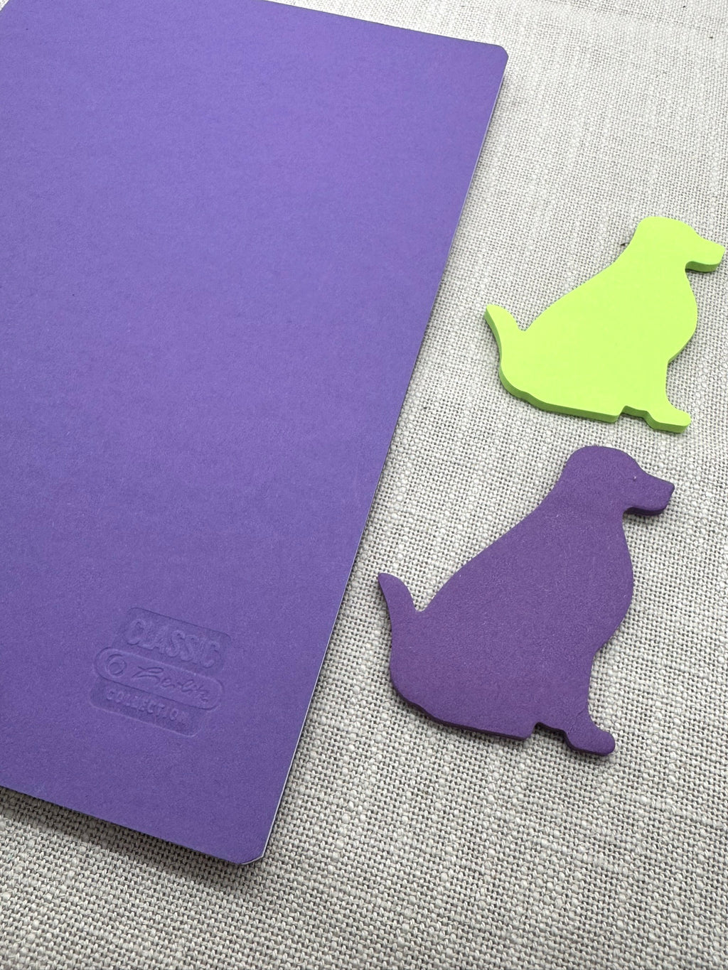 Das Herlitz Heft mit minimalistischem Cover in Lila in A4 liegt neben Haftnotizen in Hundeform.