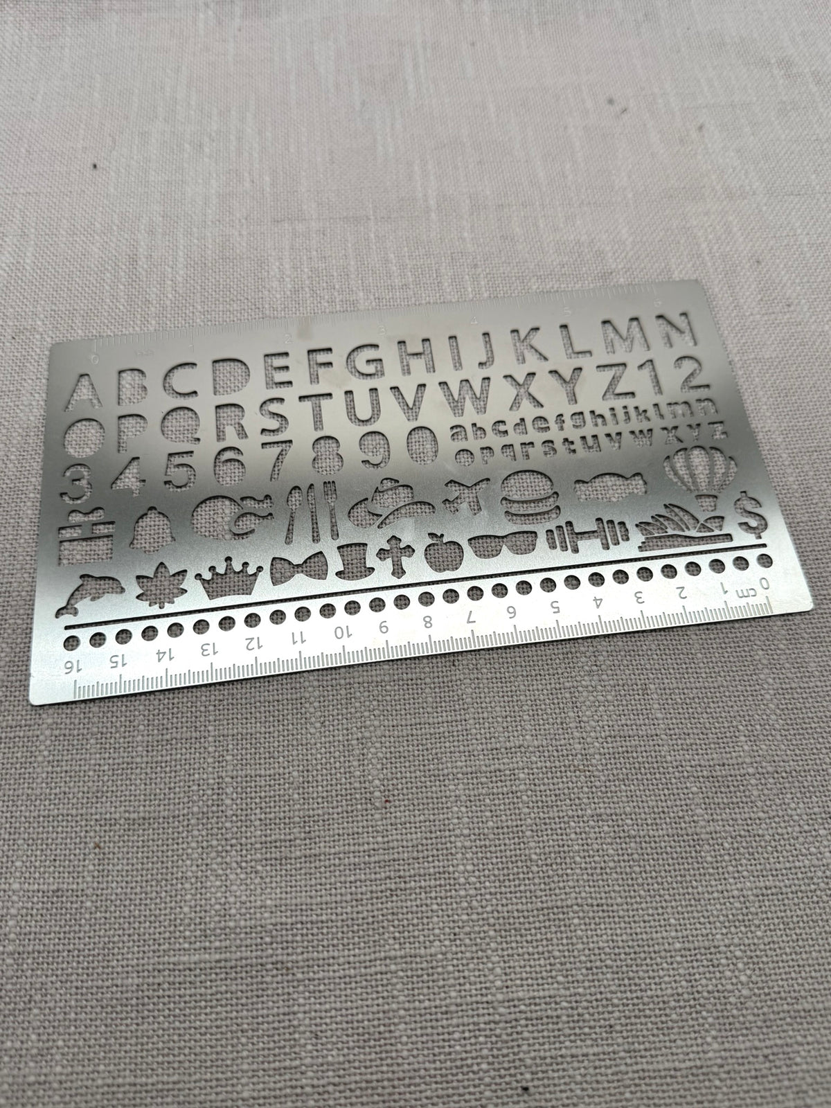 Eine Metallschablone mit großen und kleinen Buchstaben, Zahlen, Punkten und diversen Symbolen wie Geschenk, Hamburger, Hantel etc. 
