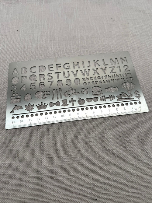 Eine Metallschablone mit großen und kleinen Buchstaben, Zahlen, Punkten und diversen Symbolen wie Geschenk, Hamburger, Hantel etc. 