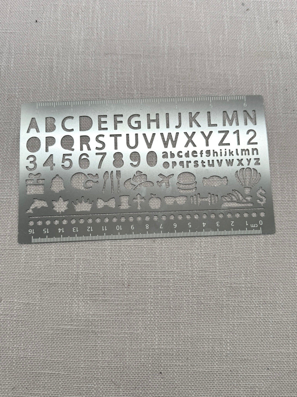 Die Metallschablone mit Buchstaben und Zahlen hat an den langen Kanten auch ein Lineal.