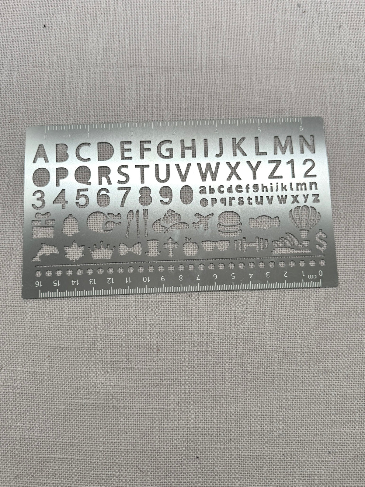 Die Metallschablone mit Buchstaben und Zahlen hat an den langen Kanten auch ein Lineal.