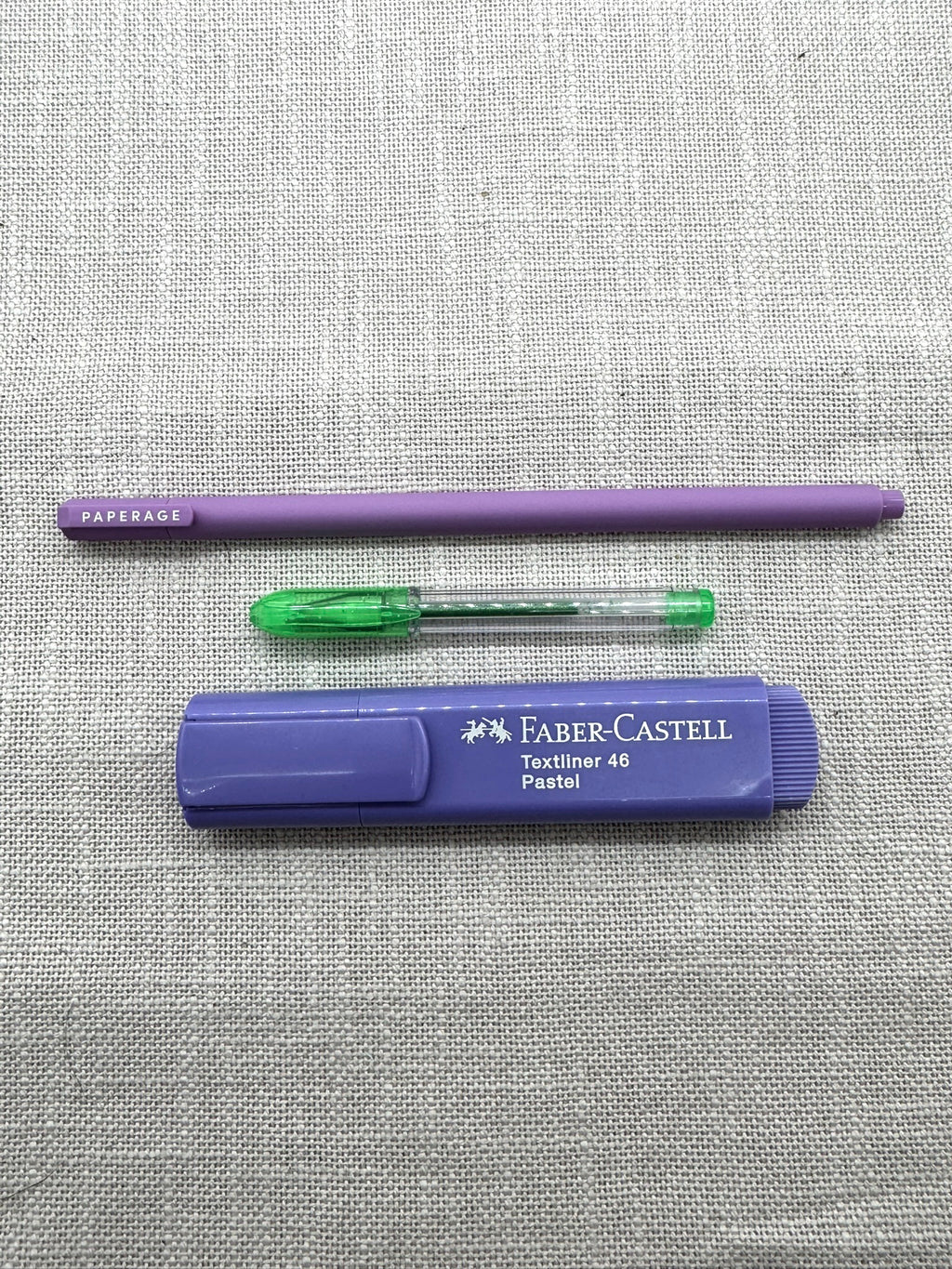 Die im Set enthaltenen Stifte nebeneinander: oben liegt der Fineliner von Paperage mit sehr feiner Spitze, iin der Mitte der kleine Gelstift in Grün, unten befindet sich der Faber-Castell Markierstift in Pastelllila