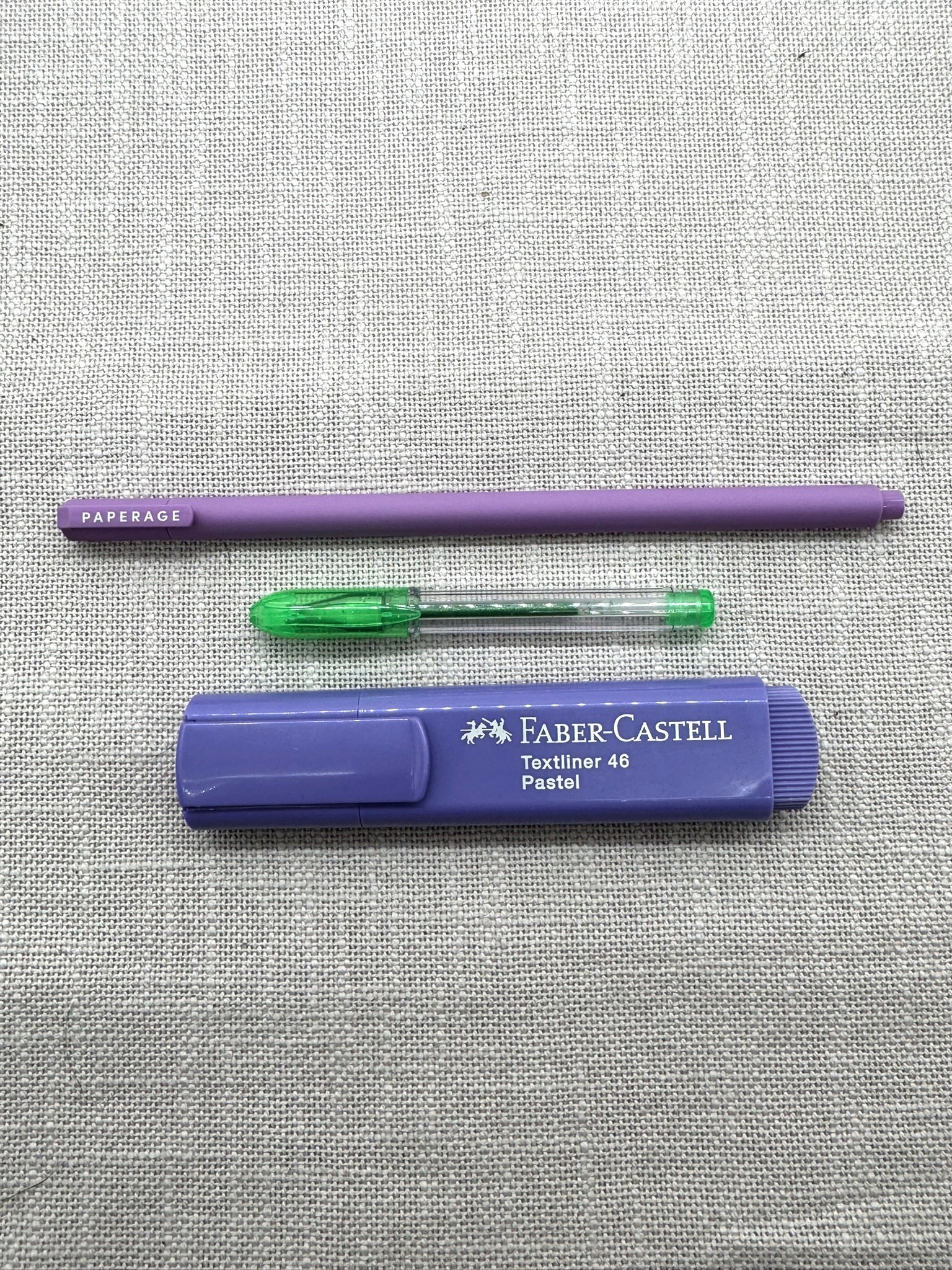 Die im Set enthaltenen Stifte nebeneinander: oben liegt der Fineliner von Paperage mit sehr feiner Spitze, iin der Mitte der kleine Gelstift in Grün, unten befindet sich der Faber-Castell Markierstift in Pastelllila