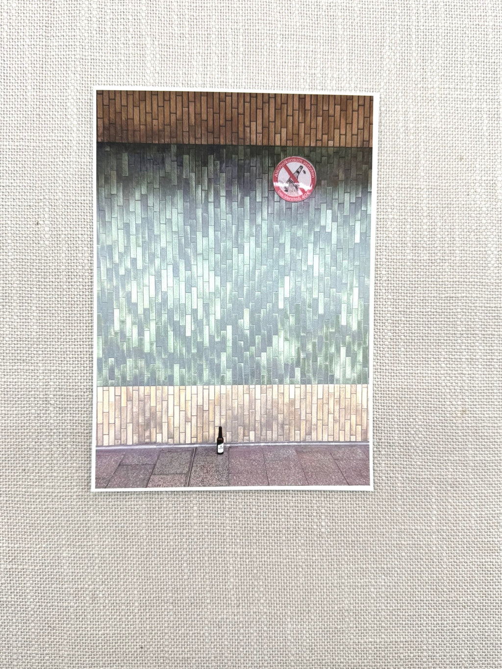 Foto einer Postkarte: Eine Veltins-Flasche steht vor einer hässlichen, gekachelten Wand einer U-Bahn Station. 50er Jahre Fliesen-Charme.