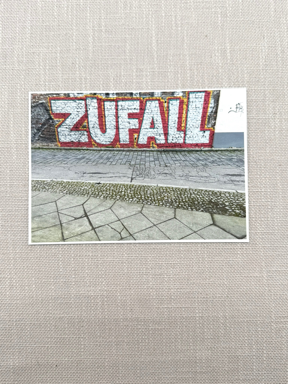 Ein zwischen Berlin-Mitte und Friedrichshain aufgenommenes Bild von Street Art. "Zufall" steht in großen silbernen Buchstaben auf einer Häuserwand.
