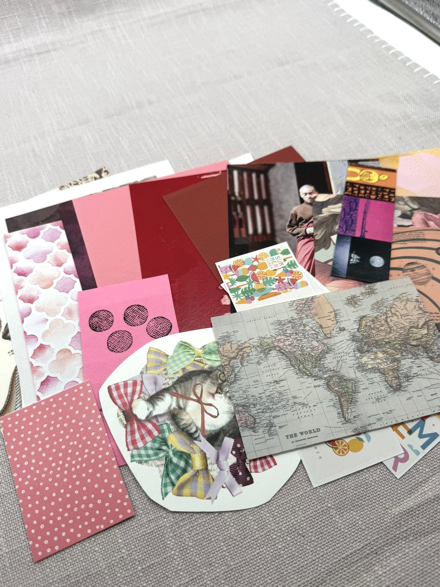 Gemischte Papierstücke aus dem Set: eine Weltkarte, ein Katzenfoto, Etiketten, Sticker, Zeitungsausschnitte, Designpapier farblich abgestimmt. 