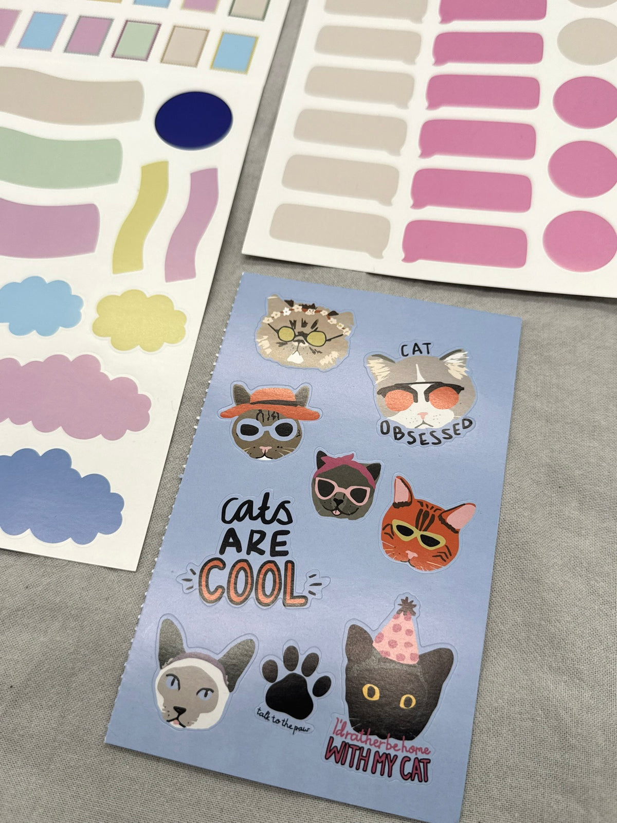 Sticker Sheets liegen nebeneinander auf hellem Hintergrund. Im Vordergrund sieht man diverse Katzenmotive. 