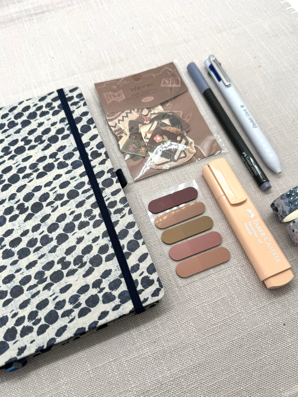 Schreibset mit einem Notizbuch, index-Streife, Sticker-Set, Textmarker, Fineliner, 4-Farben-Kugelschreiber und Washi Tapes - die einzelnen Schreibwaren sind ordentlich nebeneinander ausgelegt. Sie liegen auf einem hellen Hintergrund. 