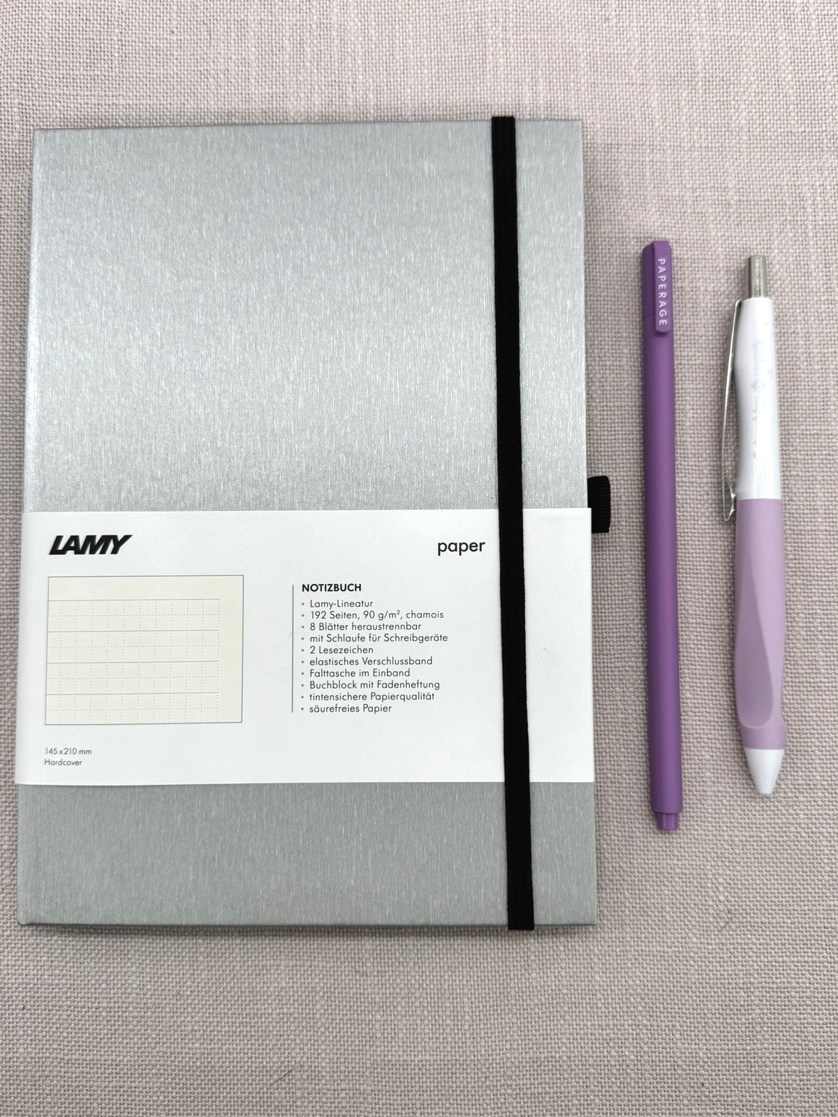 Ein silbernes Notizbuch von Lamy liegt neben zwei Stiten. 
