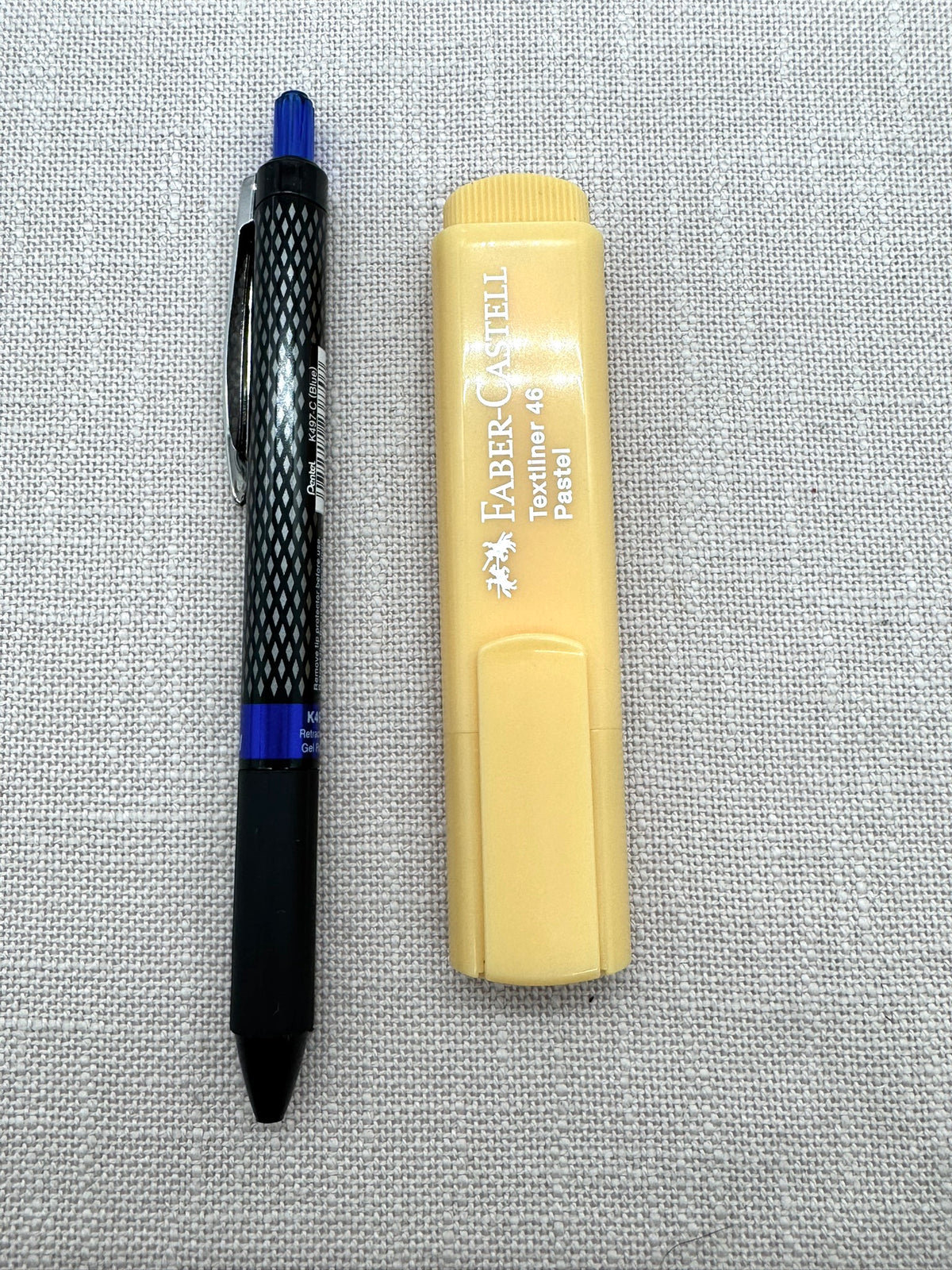 Nahaufnahme der beiden Stifte nebeneinander. Der Gelpen hat ein netzartiges Muster und eine blaue Kappe auf dem Druckmechanismus. Der Marker ist kleiner als der Stift und eckig. 