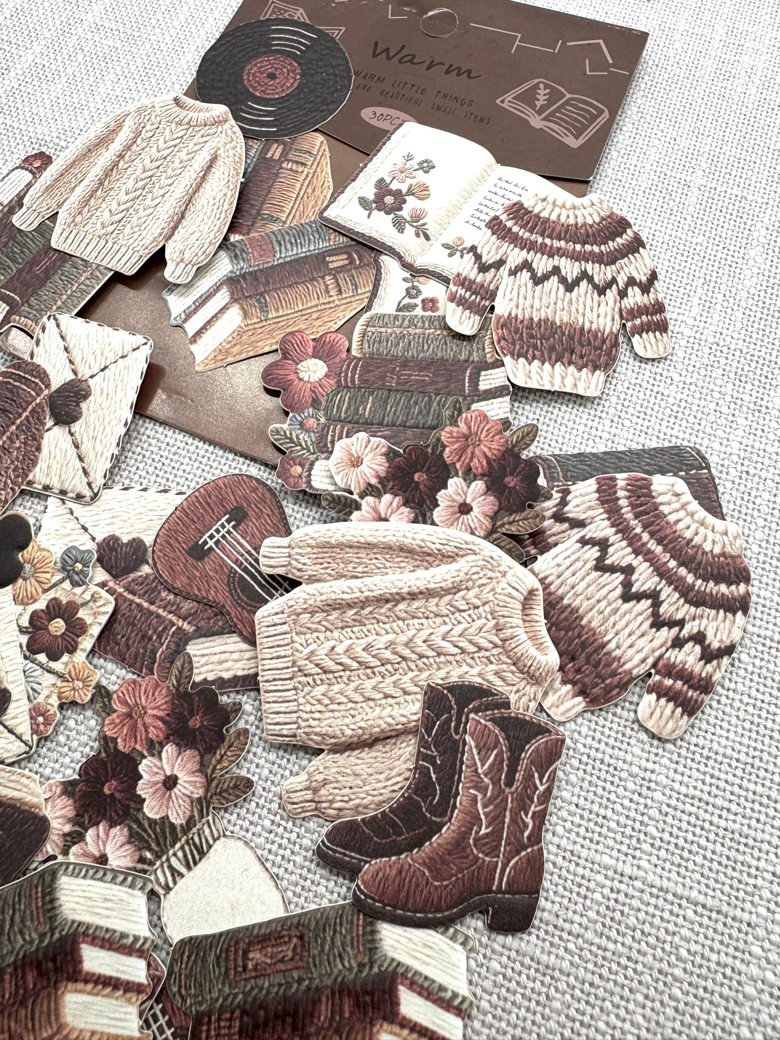 diverse Sticker verteilt auf einem hellen Hintergrund: Norweger-Pullover, Stiefel, Bücher, Gitarre, Briefumschläge, Blumen, Schalplatte. 