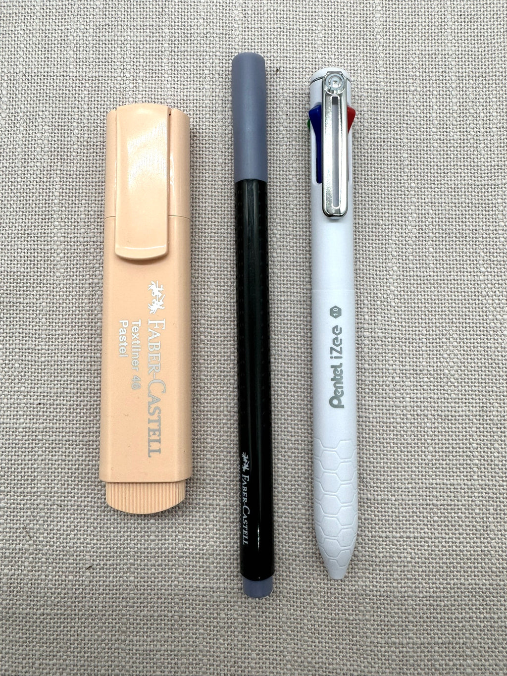 Die Stifte aus dem Set nebeneinander: ein Textmarker von Faber-Castell in Pastell, ein Fineliner in Grau, Pentel iZee mit vier Farben. 