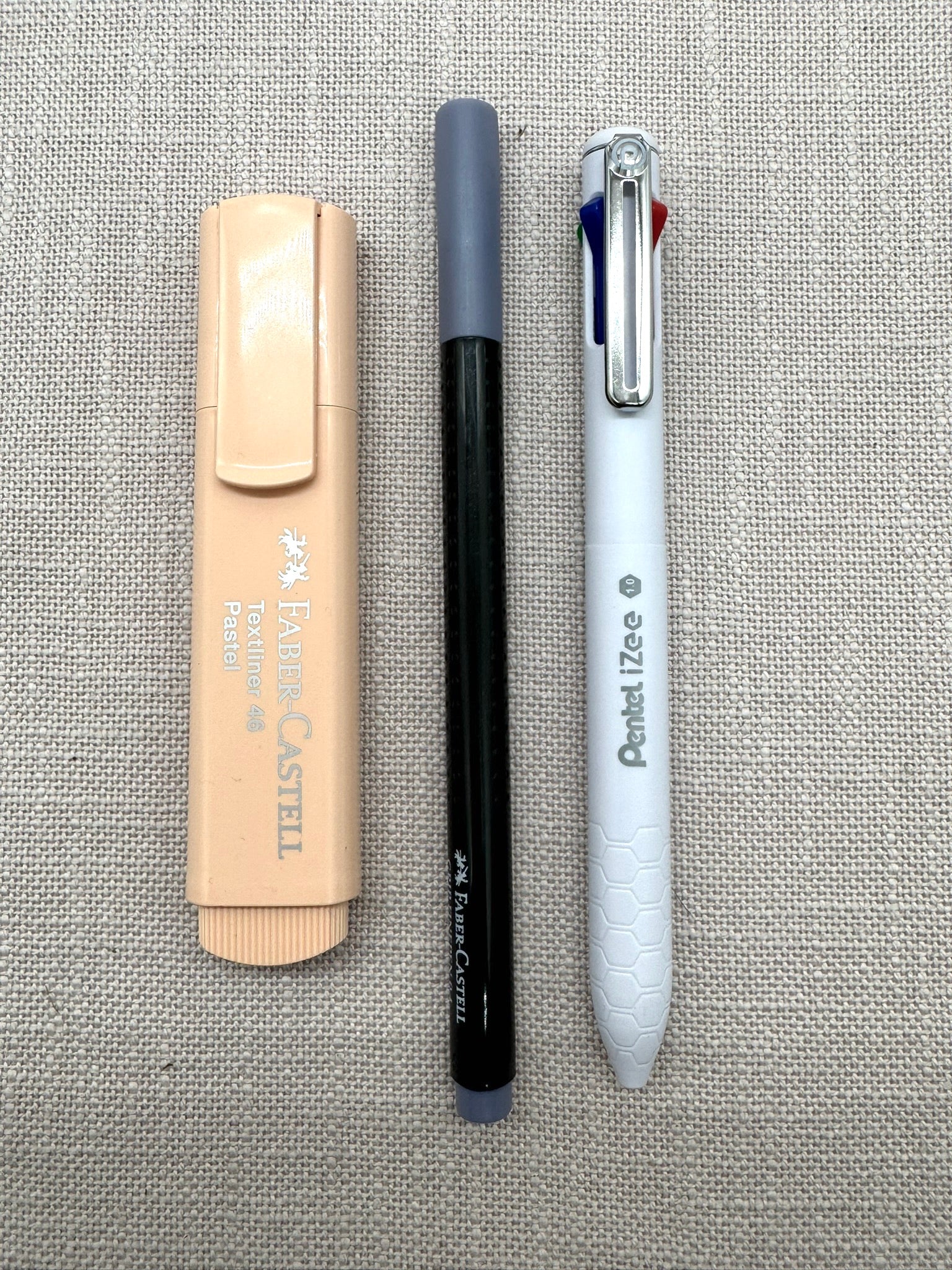 Die Stifte aus dem Set nebeneinander: ein Textmarker von Faber-Castell in Pastell, ein Fineliner in Grau, Pentel iZee mit vier Farben. 