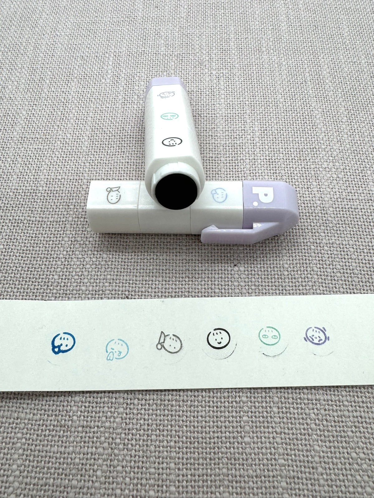 Die Stempel kann man zu einem Stift zusammenstecken. Man sieht die Motive auf einem Zettel: verschiedene kleine Gesichter. 