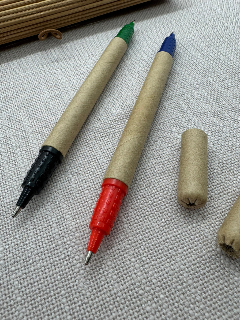 Nahaufnahme der im Set enthaltenen Kugelschreiber: der Kugelschreiber aus Pappe hat eine schwarze Spitze und eine grüne Spitze, der zweite hat eine rote Spitze und eine blaue. Beide Kappen sind ebenfalls aus Pappe. 