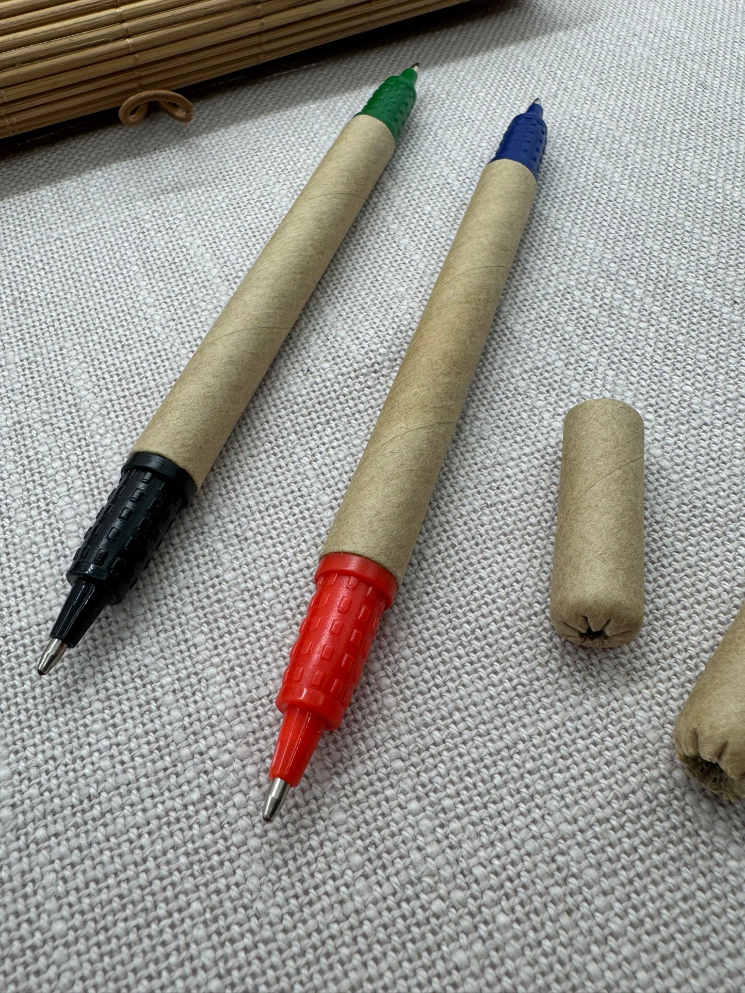 Nahaufnahme der im Set enthaltenen Kugelschreiber: der Kugelschreiber aus Pappe hat eine schwarze Spitze und eine grüne Spitze, der zweite hat eine rote Spitze und eine blaue. Beide Kappen sind ebenfalls aus Pappe. 